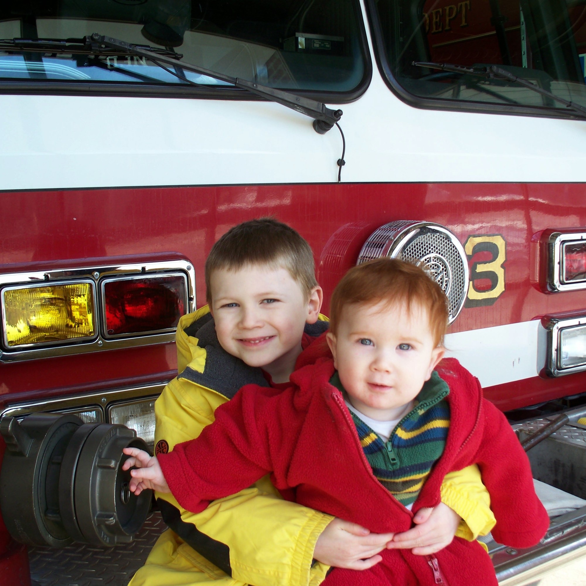 two young boys in front of a fire truck, one carrying a fire hydrant