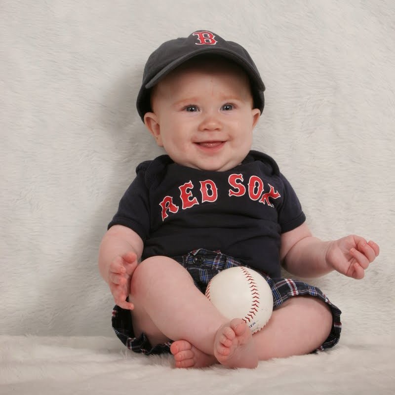 The image shows a baby wearing a Red Sox hat and shirt, holding a baseball.