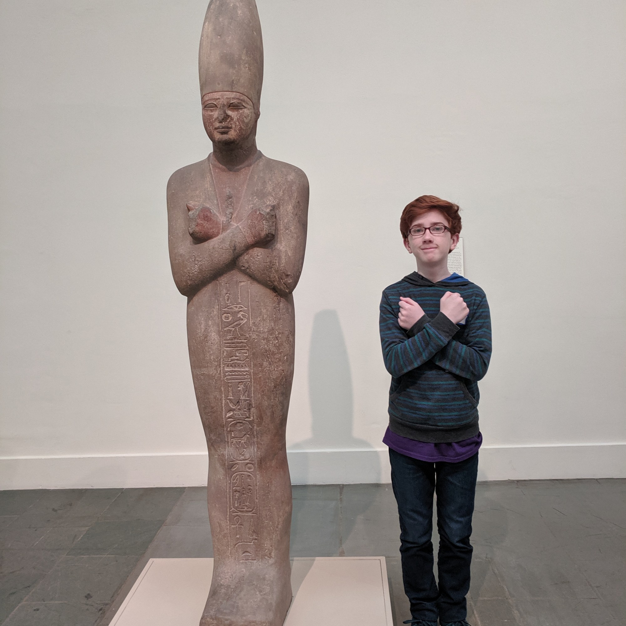 An individual stands next to a large ancient Egyptian statue. Ancient Egyptian relief-like hieroglyph symbols can be seen ...